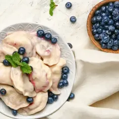 Pyszne pierogi z borówkami amerykańskimi, ozdobione świeżymi jagodami i miętą, prezentują się apetycznie na talerzu.