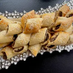 Paszteciki z pieczarkami i serem, posypane sezamem, ułożone na ozdobnej tacy z kwiatowymi zdobieniami.