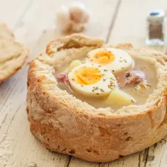 Gotowy zakwas na żurek w chlebie, z jajkiem i ziemniakami. Obok kromka chleba i przyprawniki.