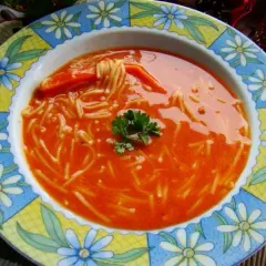 Zupa pomidorowa z przecieru z makaronem nitki i natką pietruszki, podana w kolorowym talerzu.