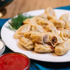 Pyszne pierogi z gęsiną, podane z ziołowym dipem i sosem pomidorowym, ozdobione gałązką koperku.