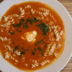 Pyszna zupa pomidorowa jak u mamy, z makaronem i kleksem śmietany, posypana natką pietruszki.
