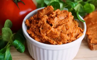 Pyszna, domowa pasta z soczewicy w białej miseczce, obok pomidora i świeżej zieleniny. Idealna na kanapki.
