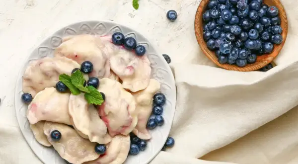 Pyszne pierogi z borówkami amerykańskimi, ozdobione świeżymi jagodami i miętą, prezentują się apetycznie na talerzu.