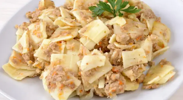 Łazanki z mięsem, kapustą i pieczarkami, udekorowane natką pietruszki, na białym talerzu.