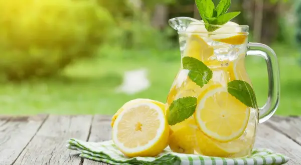 Jak zrobić dobrą lemoniadę? Orzeźwiający napój z cytryn, lodu i mięty w dzbanku, na drewnianym stole.