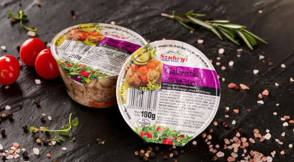 Dwie galaretki drobiowe Szubryt na czarnym tle, otoczone pomidorkami, ziołami i przyprawami. Wartość odżywcza: 233 kJ/55 kcal.