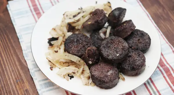 Kaszanka pokrojona w plastry z podsmażoną cebulą na białym talerzu.