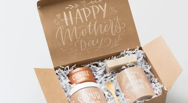 Otwarty brązowy karton z napisem "Happy Mother's Day" i zawartością: świeca, peeling, mydło, kubek i drewniana łyżeczka.