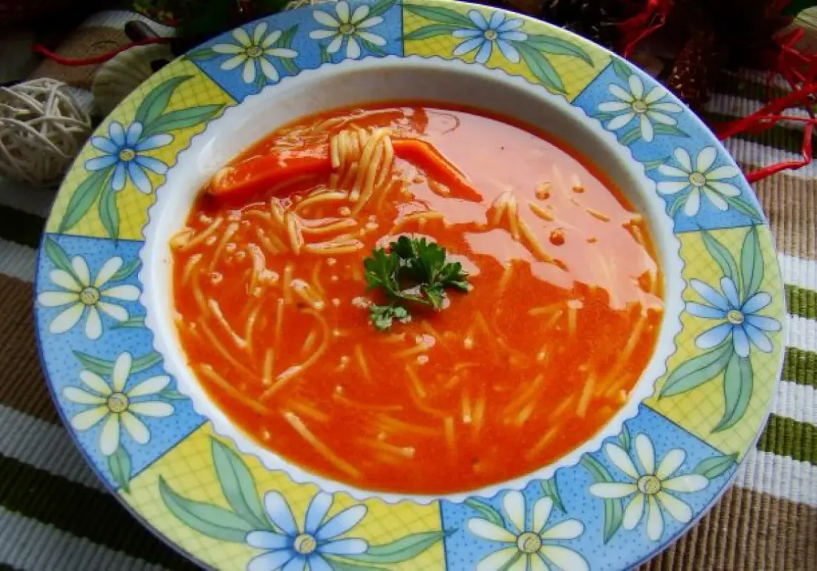 Zupa pomidorowa z przecieru z makaronem nitki i natką pietruszki, podana w kolorowym talerzu.