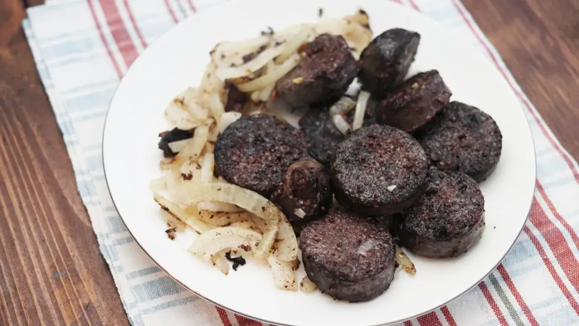 Kaszanka pokrojona w plastry z podsmażoną cebulą na białym talerzu.
