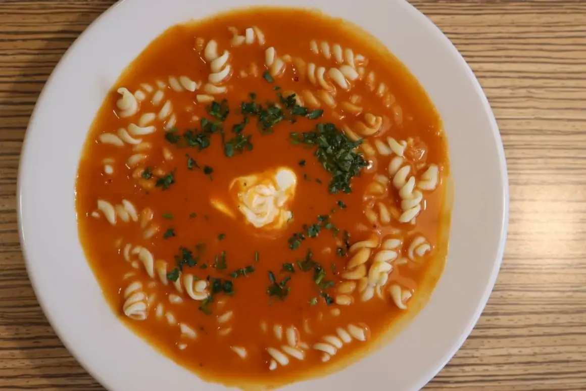 Pyszna zupa pomidorowa jak u mamy, z makaronem i kleksem śmietany, posypana natką pietruszki.