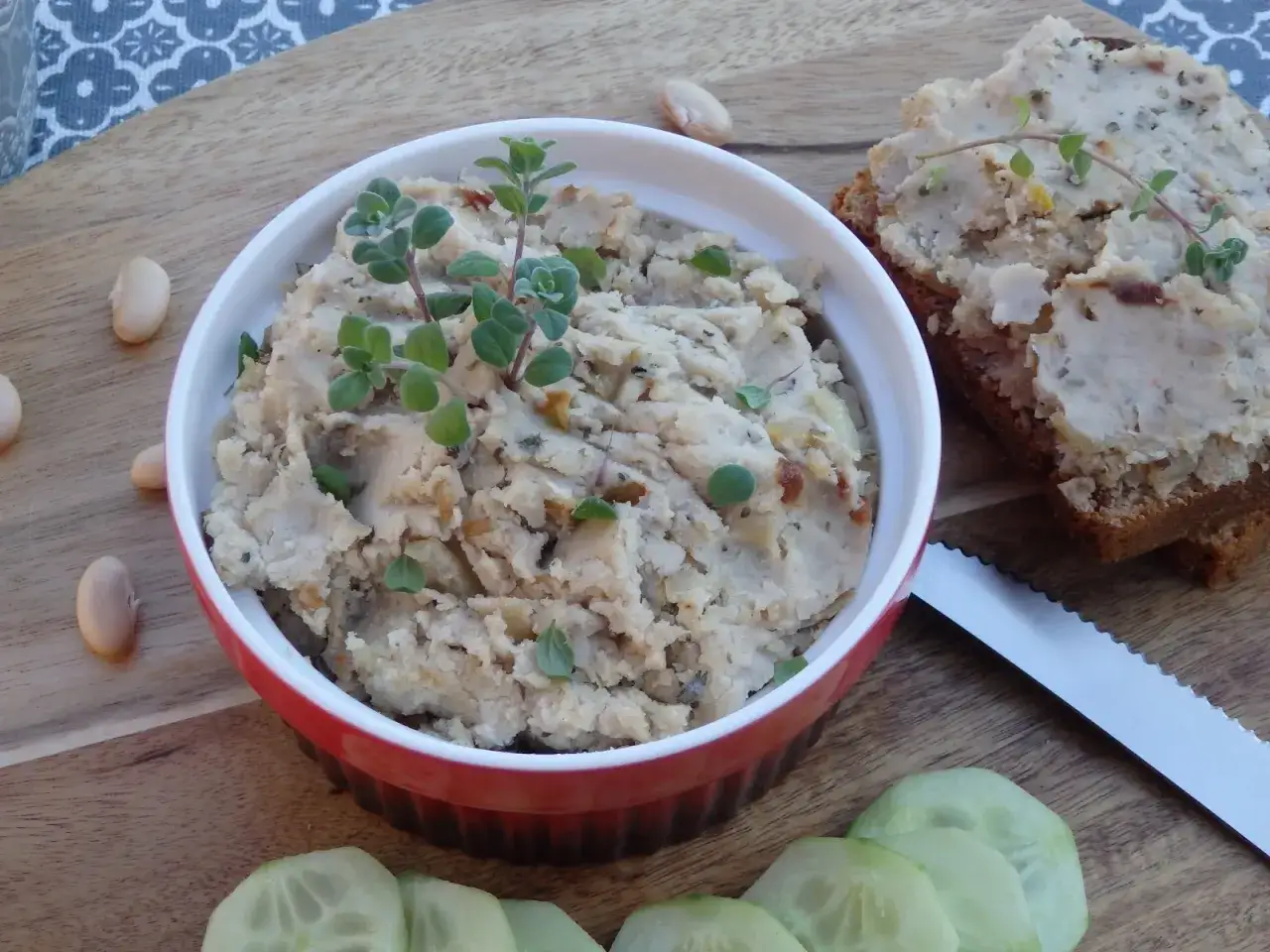 Pyszna pasta z białej fasoli, udekorowana świeżymi ziołami, podana z chlebem i ogórkiem.