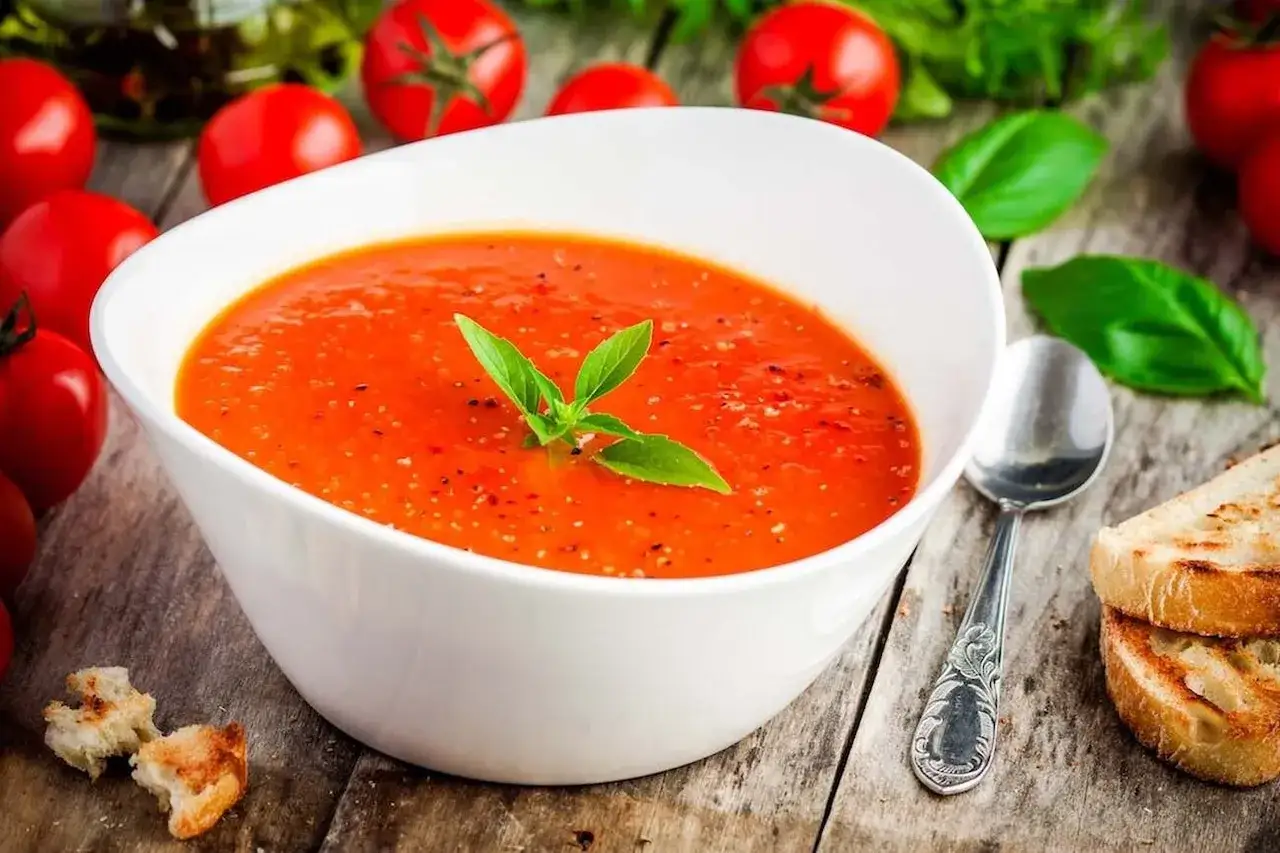 Aksamitna zupa pomidorowa jak u mamy, ozdobiona listkiem bazylii, podana z chrupiącymi grzankami.