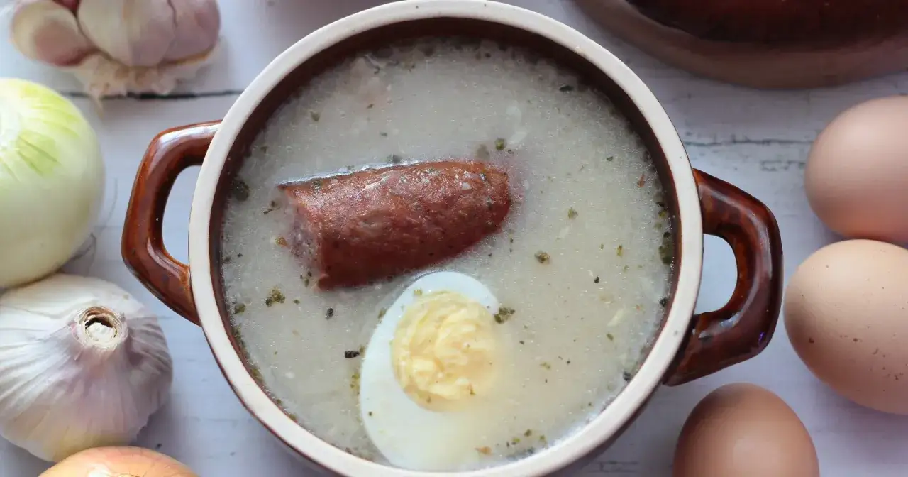 Aromaticzny żur na zakwasie z kiełbasą i jajkiem, otoczony czosnkiem i cebulą.
