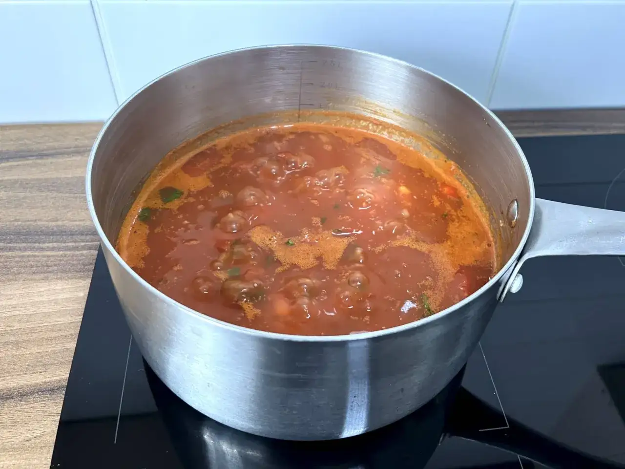 Gotuje się aromatyczna zupa pomidorowa na kostce. W garnku bulgocze gęsty, czerwony sos z kawałkami pomidorów i zieleniną.