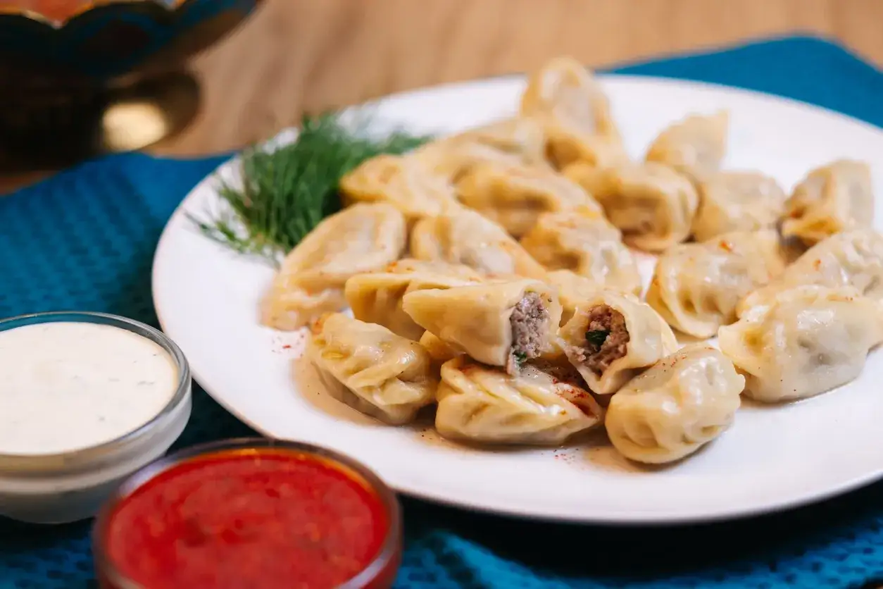 Pyszne pierogi z gęsiną, podane z ziołowym dipem i sosem pomidorowym, ozdobione gałązką koperku.