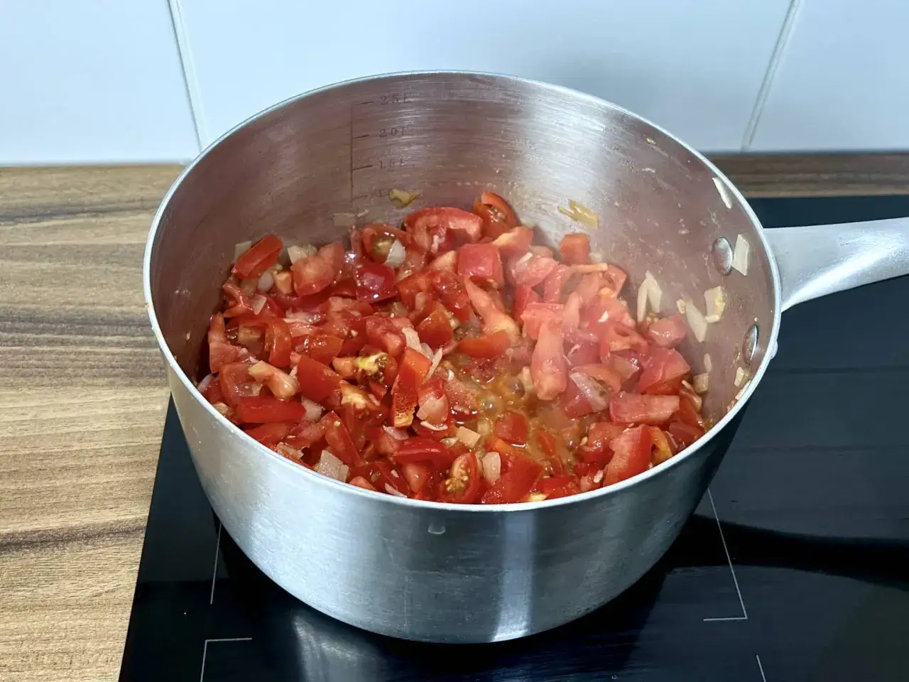 Gotuje się zupa pomidorowa na kostce. Pokrojone pomidory i cebula w metalowym garnku na płycie indukcyjnej.